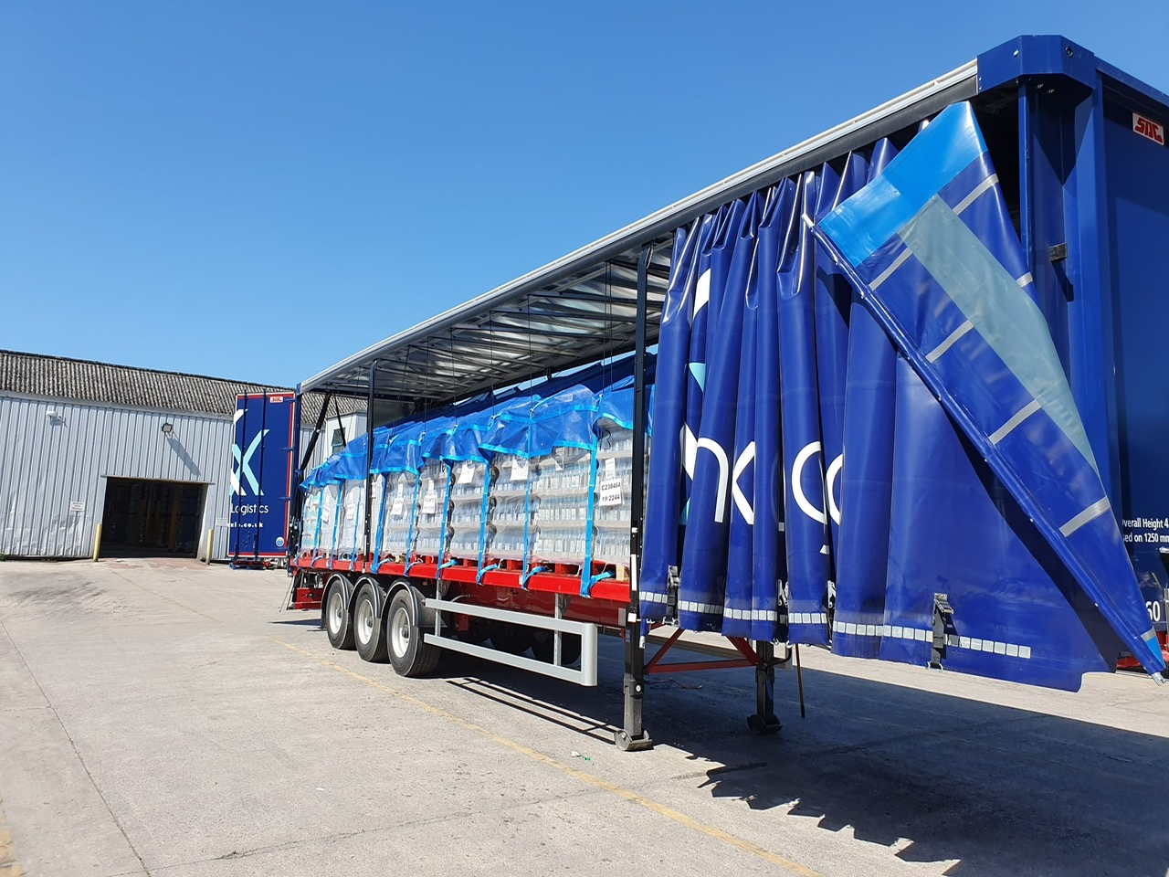 KX Logistics artic with kite covers over bottled freight in a depot yard